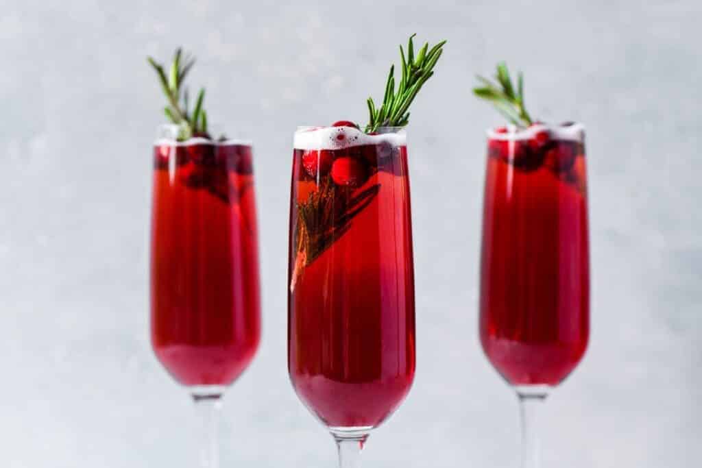 Poinsettia Cocktail glasses along with the fresh red cherries and rosemarry leaves