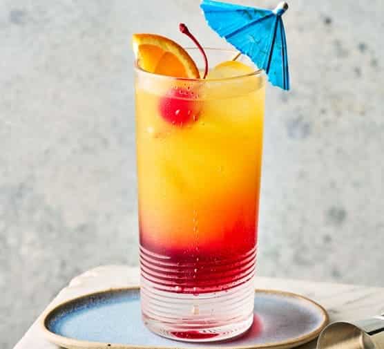 a chilled glass of Tequila Sunrise garnish with straw umbrella and fresh orange slice and cherry