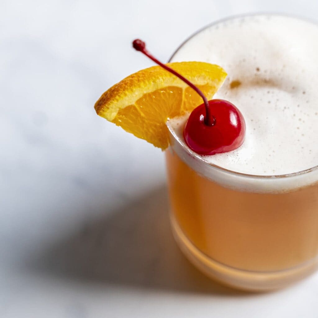 a glass of Amaretto Sour drink along with the fresh orange chunk and fresh red cherry on top