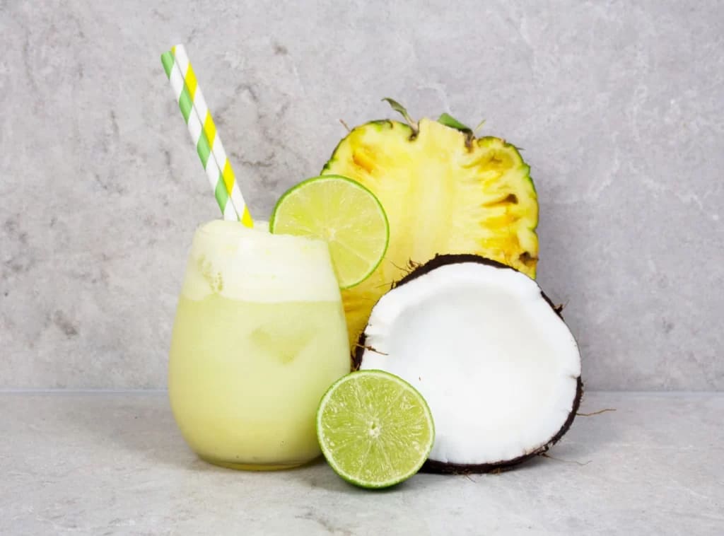 a glass of Lime Infused Coconut Spritzer with fresh coconut pineapple and lime wedges