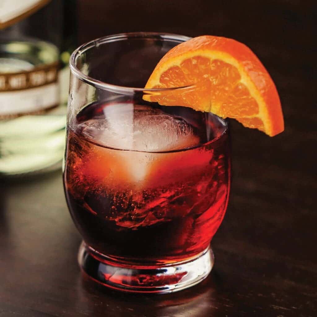 a glass of Mezcal Negroni cocktail served with fresh orange slice