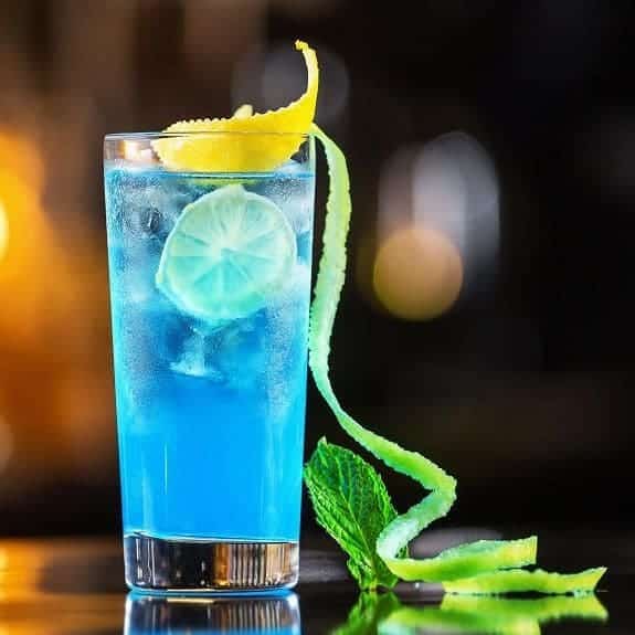 a glass of blue lagoon served with lemon and lime peel along with lemon wedges