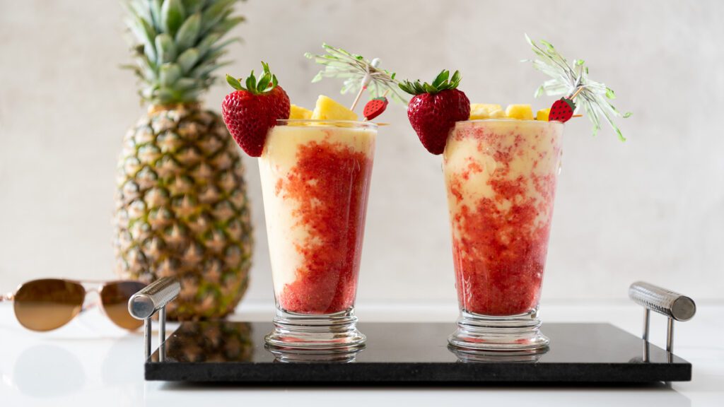 glasses of Mocktail of Virgin Lava Flow served with fresh pineapple chunks and strawberries along with the whole pineapple and goggles on side