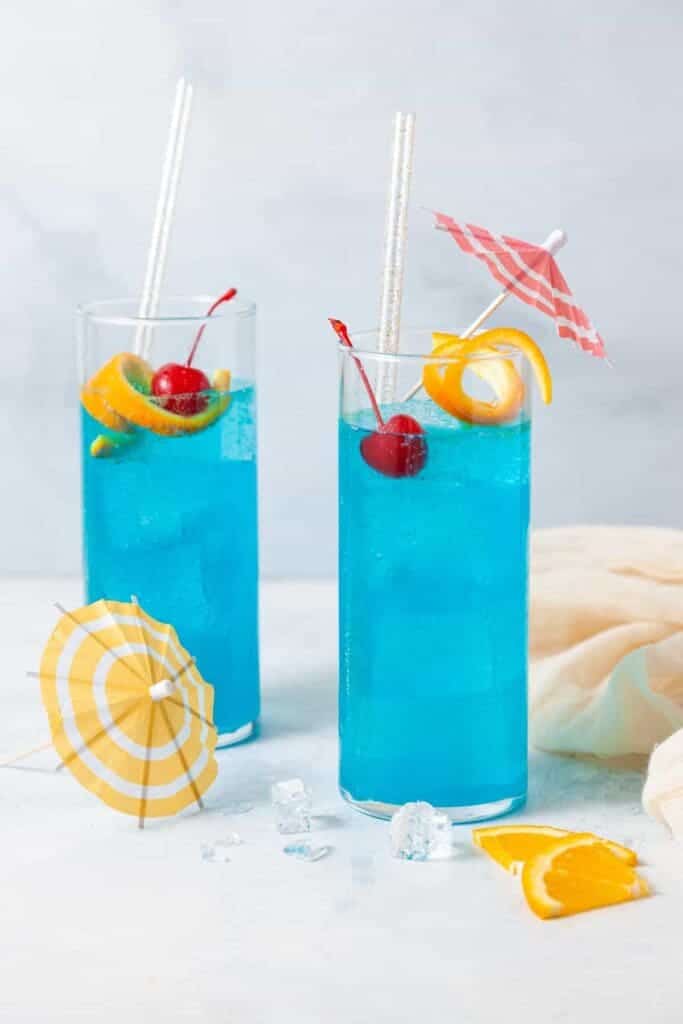 glasses of blue lagoon mocktail garnish with lemon orange peel and cherry