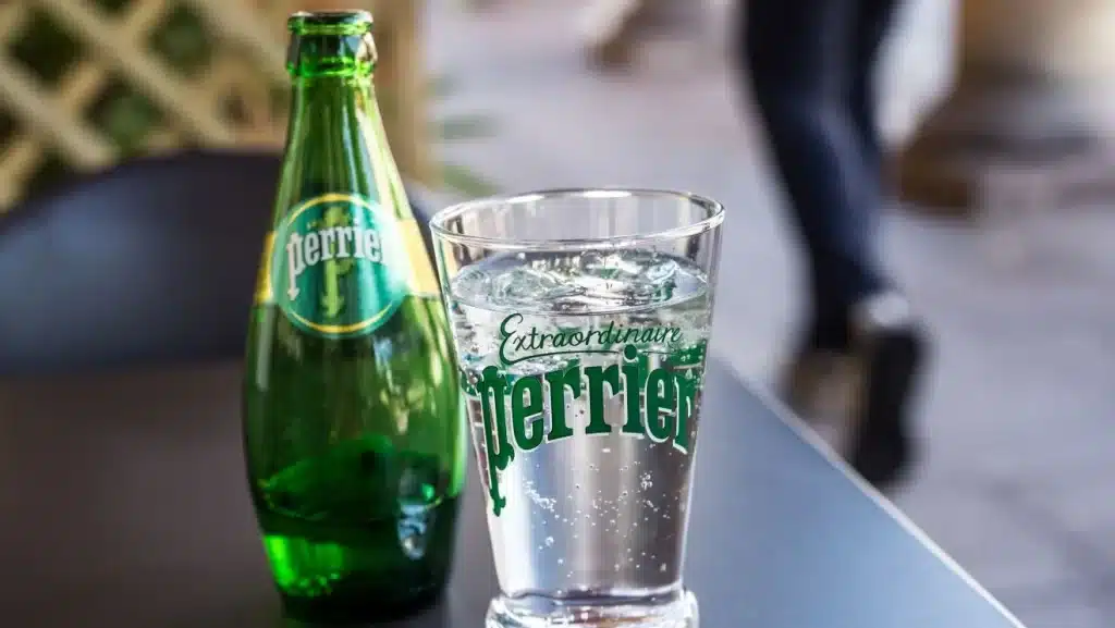 a dark green bottle and glass of perrier water