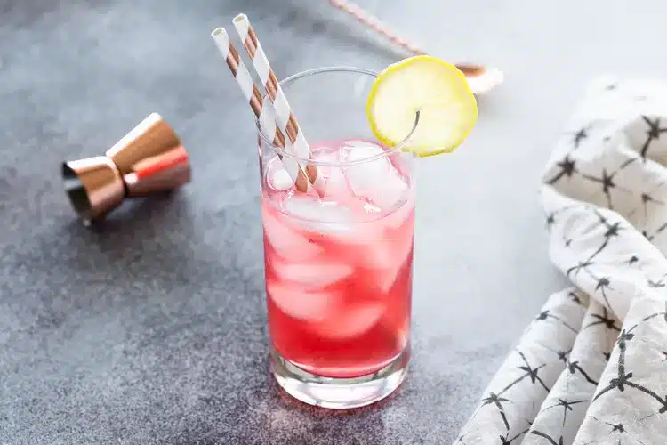 a glass of cranberry iced tea with a straw and lemon wedge