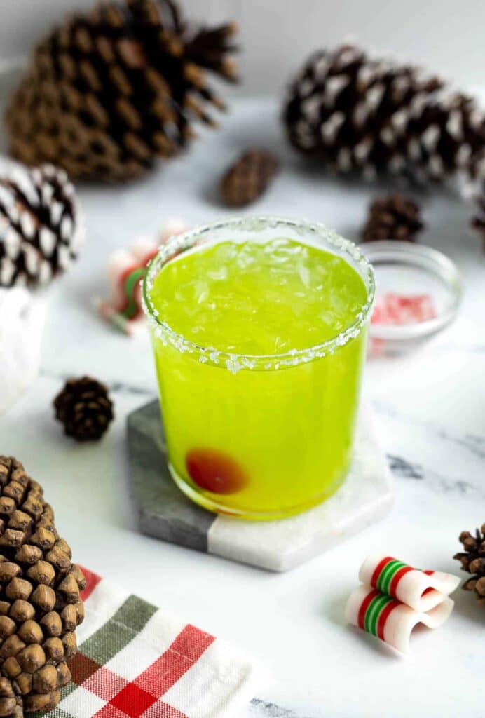 a glass of grinch mocktail placed on a marble piece with pines in the background