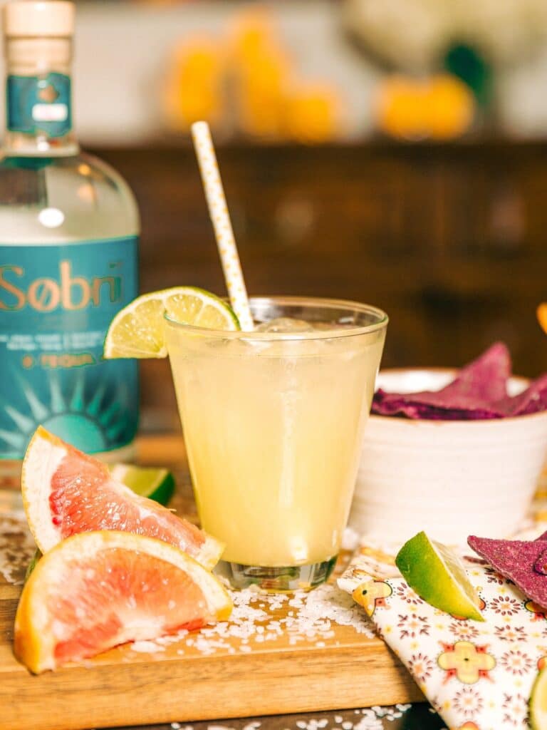 a glass of non alcoholic cantarito cocktail on a wooden tray with tequila bottle in background