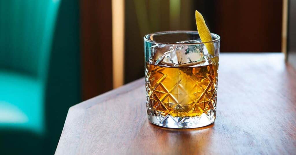 a glass of rusty nail cocktail topped with ice and lemon wedge