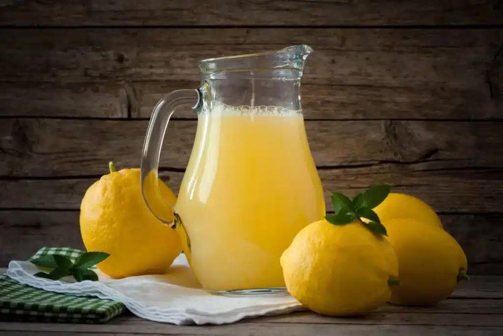 a jug of Citronnade placed on a white towel with three oranges lying nearby