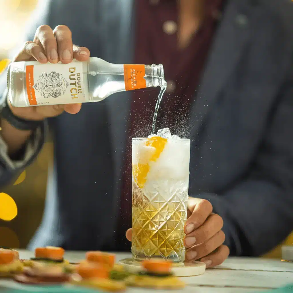 a man adding tonic water in a glass with Spiced Rum and ice