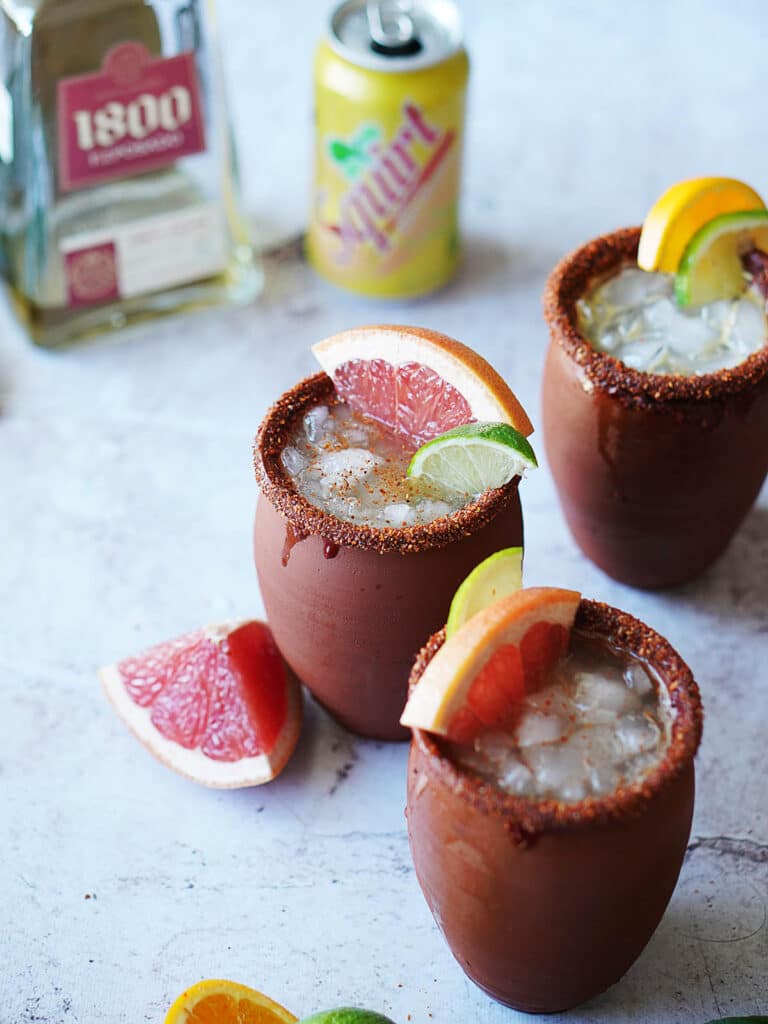 three cups of cantarito drink garnished with grapefruit wedges and lemon