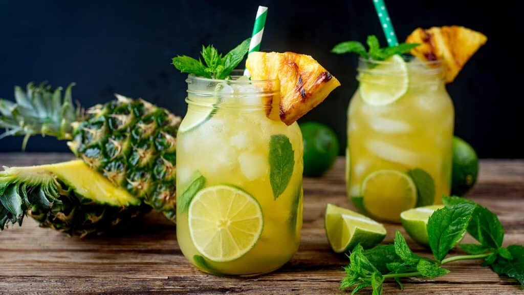 two glass of Pineapple Mojito Rum with straws inside and garnished with glazed pineapple wedges and lemons