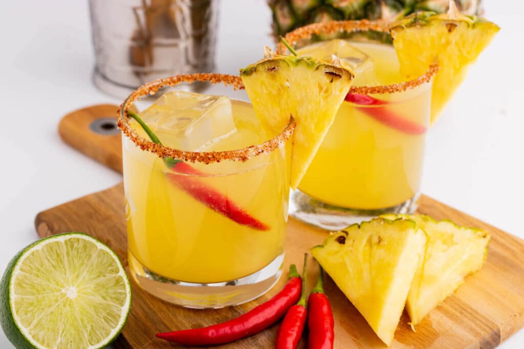 two glass of Spicy Pineapple Rum Margarita garnished with pineapple wedge and whole red chillies placed on a wooden tray