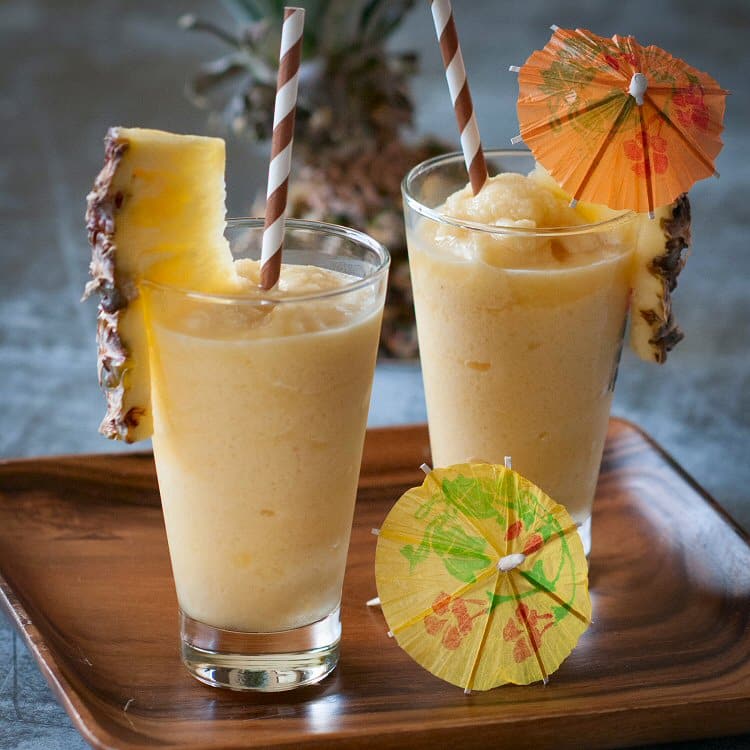 two glass of frozen pineaaple daiquiri garnished with pineapple wedges straws and decorative umbrellas