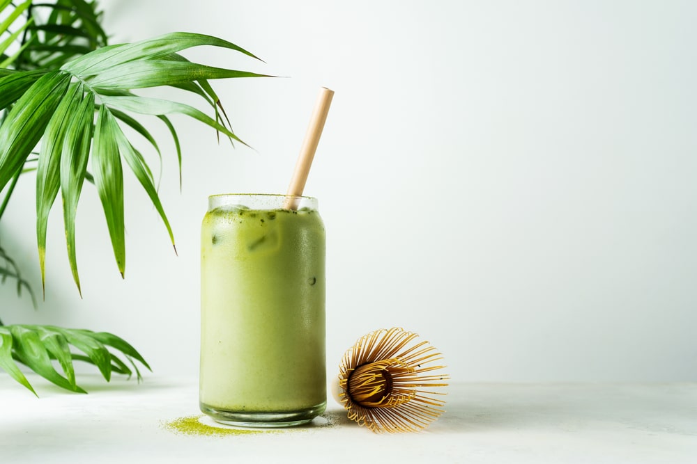 Japanese iced matcha latte green tea with milk with bamboo straw in glass on white background