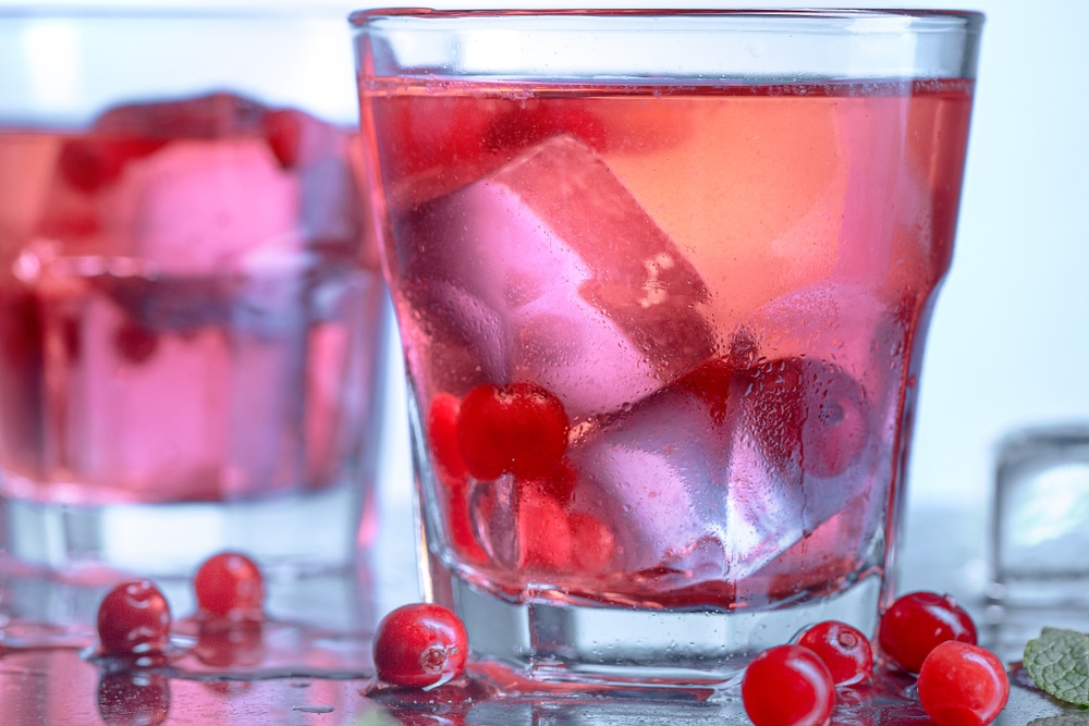 A close view of a glass of cranberries along with a cape cod drink with ice 