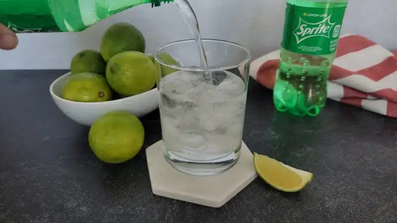 A view of a bottle of sprite being poured into a glass with lemons on the side