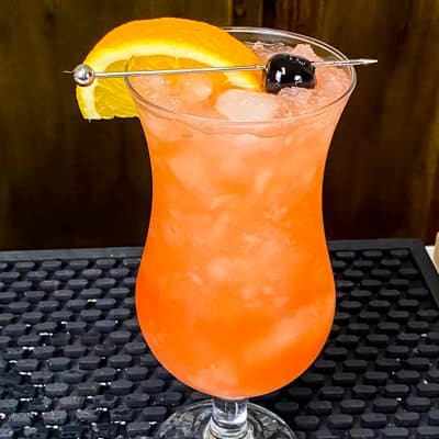 A view of a glass of hurricane drink with a cut orange on it