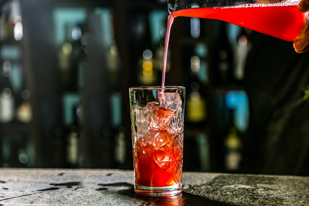 A view of a person pouring some cranberry juice inside a glass with ice