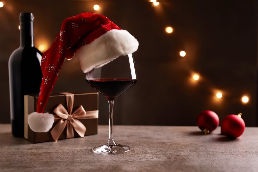 A view of a red wine glass with a Christmas hat and some gifts on the side