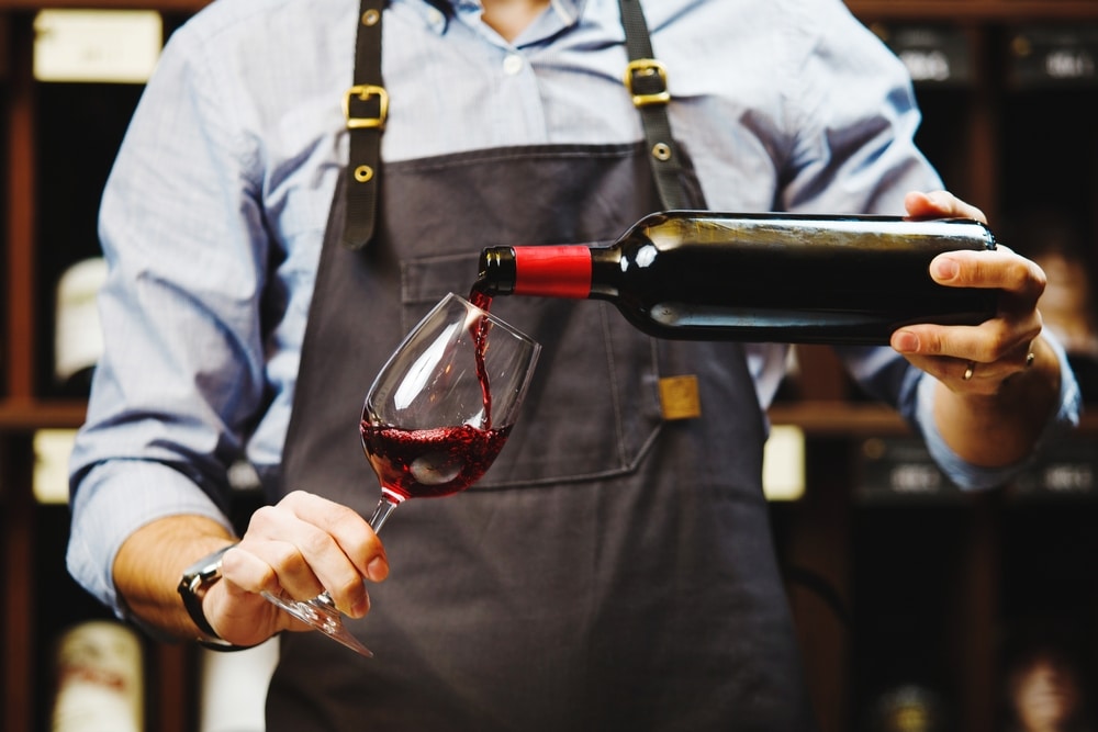 A view of a person pouring some red wine in a glass