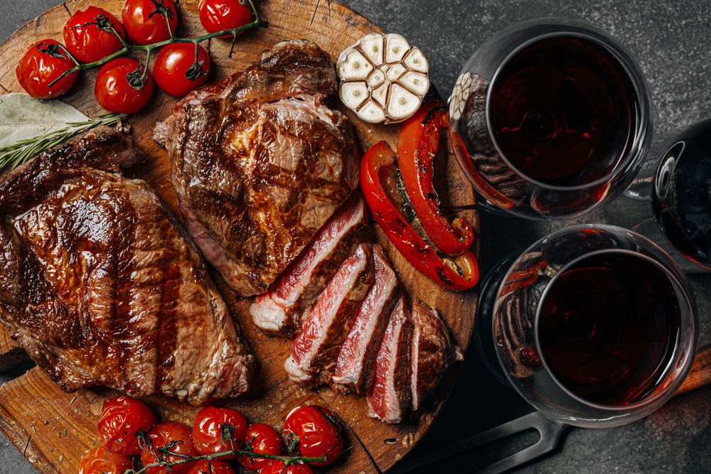 An overhead view of two glasses of wine with steak cut on board